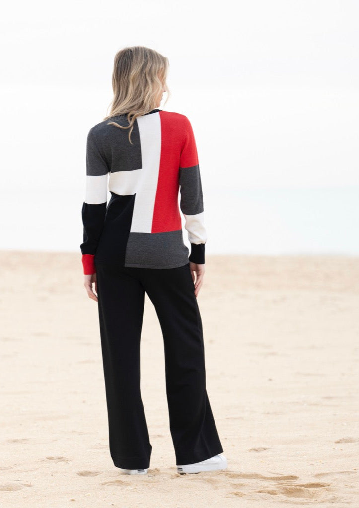 Woman wearing a colorful sweater and black pants on a sandy beach.