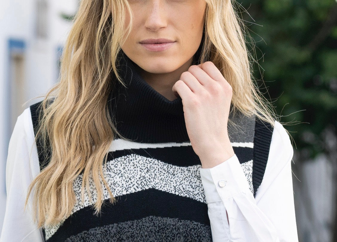 Person wearing a black and white striped sweater vest over a white shirt.