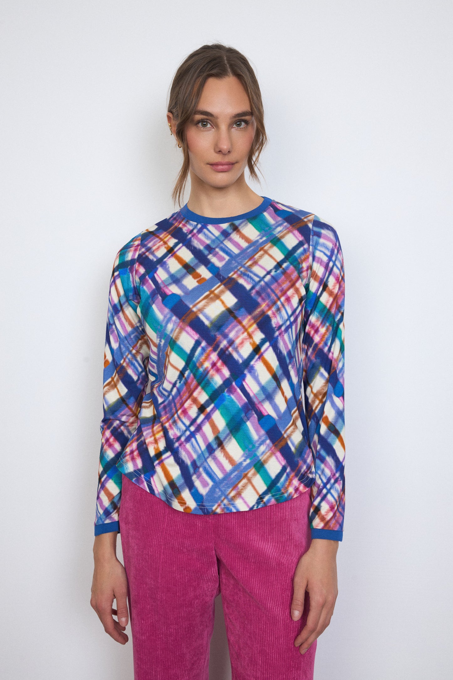 Woman wearing a colorful plaid shirt and pink pants against a white background