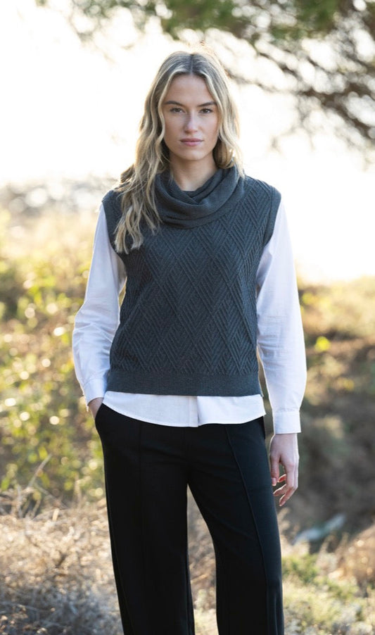 Woman wearing a dark gray sleeveless sweater over a white shirt in a natural setting