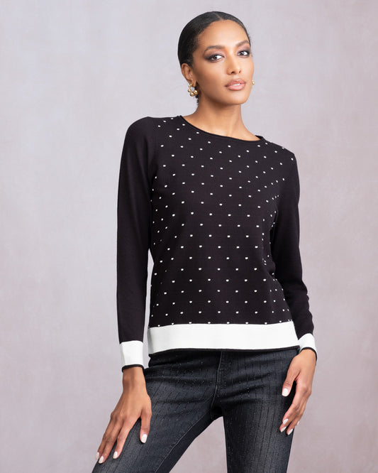 Woman wearing a black sweater with white polka dots and dark jeans on a gray background