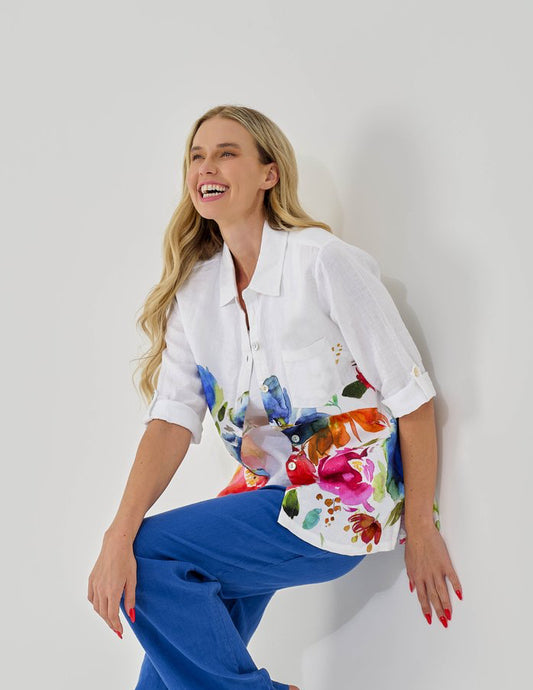 Woman wearing a white shirt with colorful floral design and blue pants on a white background