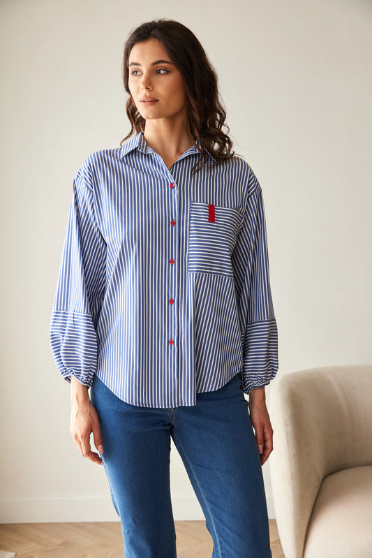 Woman wearing a blue and white striped shirt with a red pocket detail, standing in a room with a beige sofa.