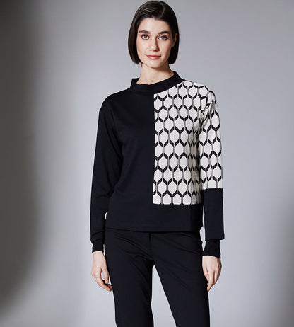 Person wearing a black and white patterned sweater with black pants on a gray background