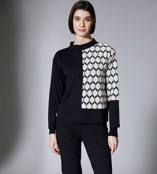 Person wearing a black and white patterned sweater with black pants on a gray background